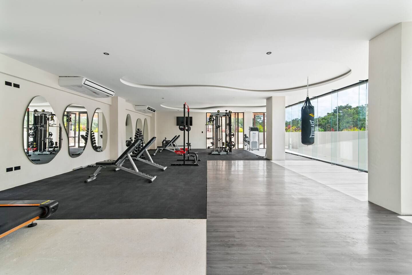 A modern gym with mirrored walls, various exercise equipment, and a punching bag.