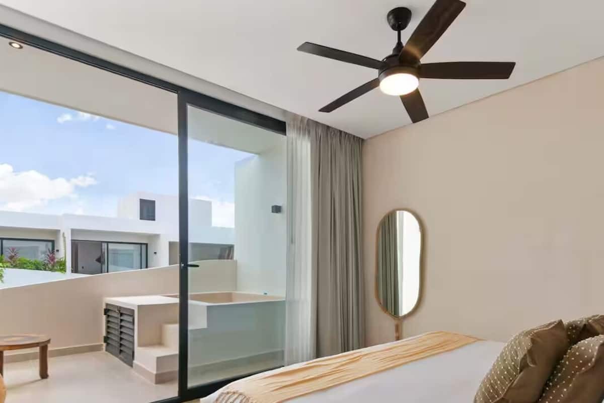 A modern hotel room with a balcony, a ceiling fan, a bed with a wooden headboard, and a large mirror.