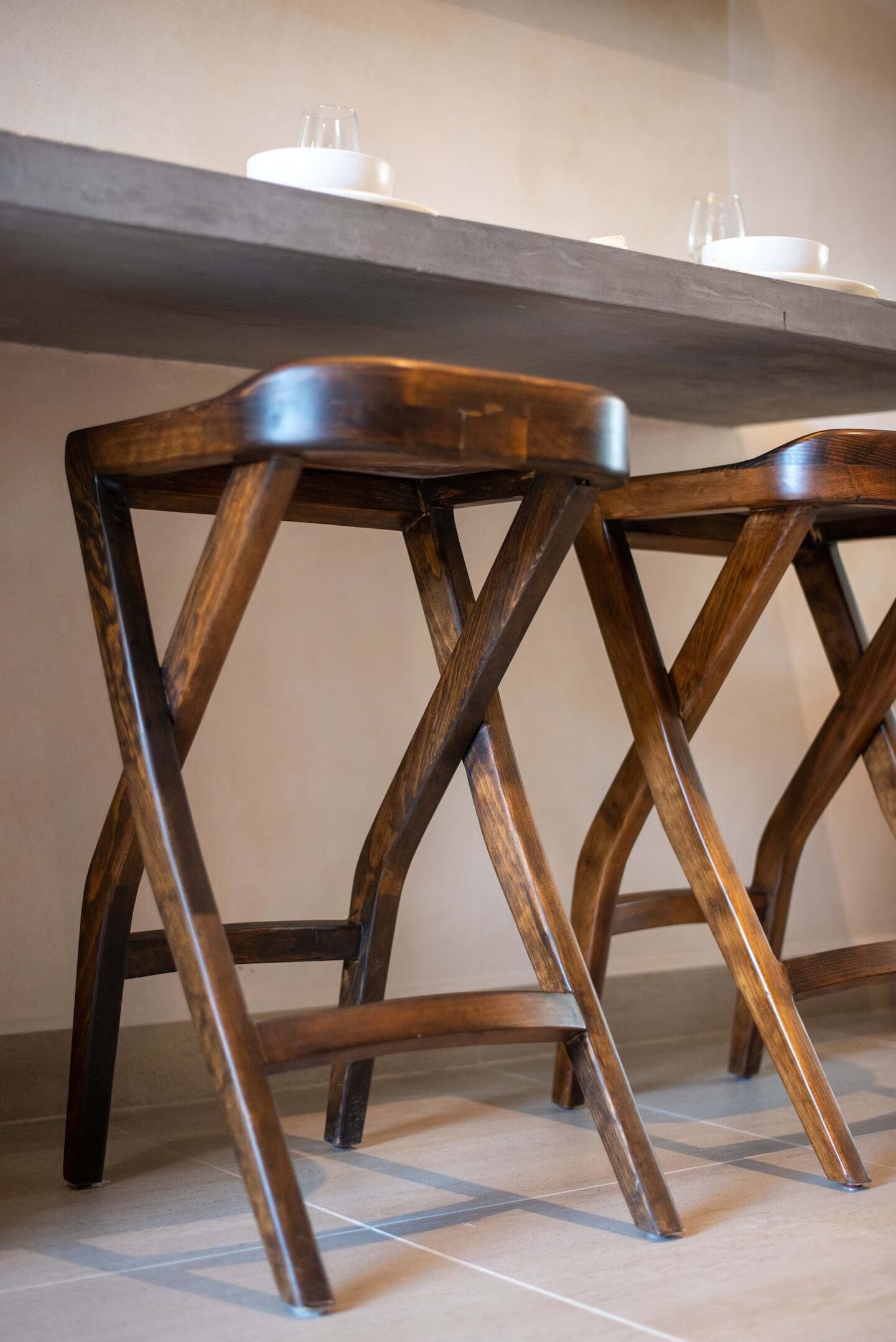 A wooden chair with a unique X-shaped backrest design, placed on a tiled floor.