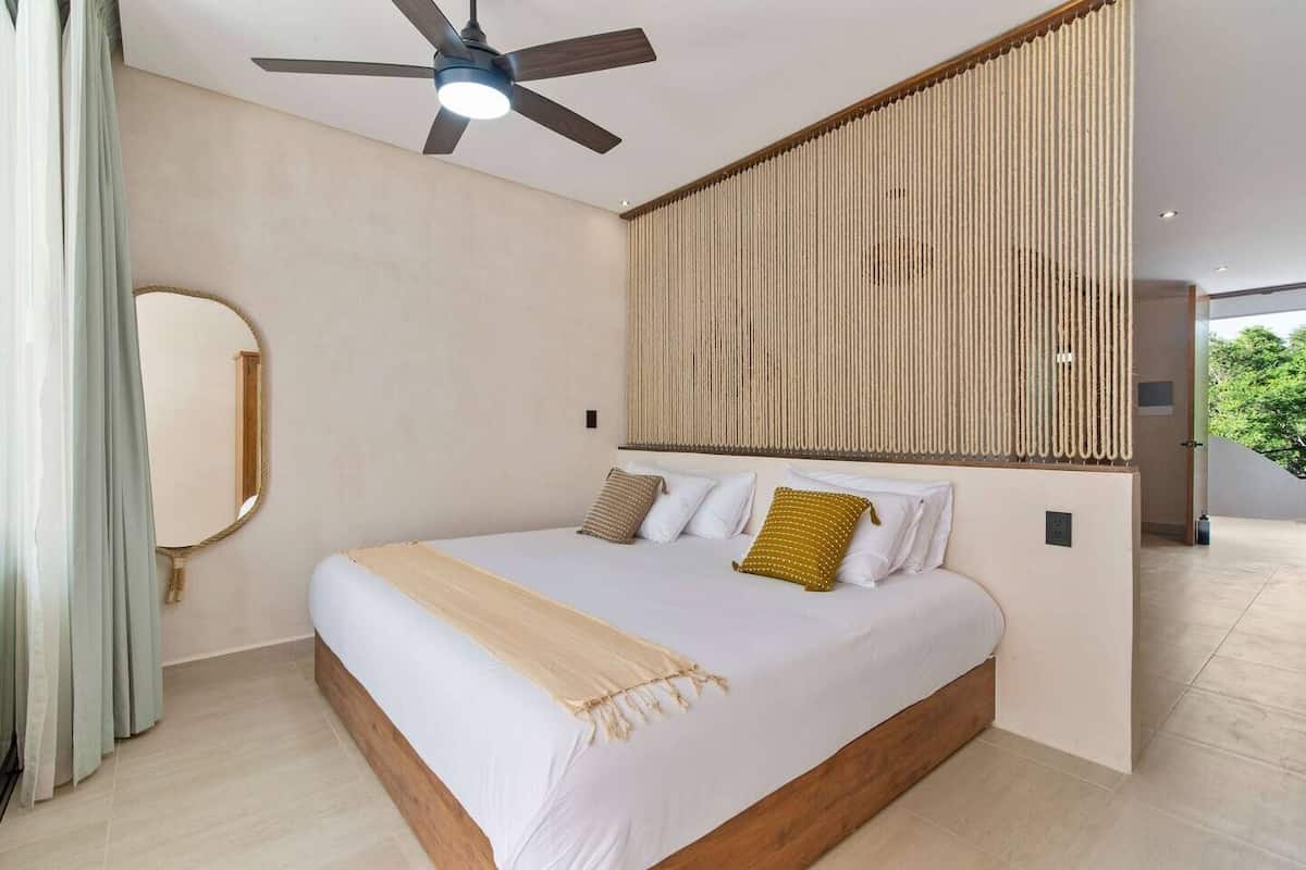 A modern bedroom with a large bed, a ceiling fan, a mirror, and a textured wall panel.