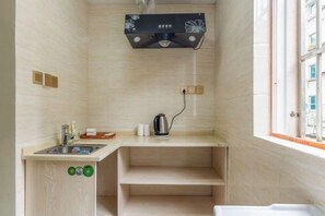 Cocina pequeña con pileta, mostrador y tetera. Se ve un ventanal con vistas a edificios.