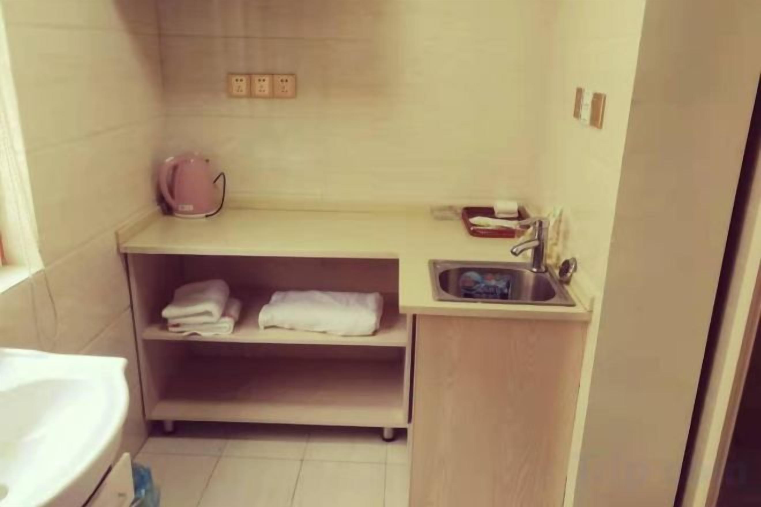 A small bathroom with a sink, a shelf with folded towels, and a pink kettle.