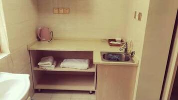A small bathroom with a sink, a shelf with folded towels, and a pink kettle.