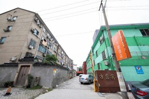 A narrow street with multi-story buildings, a visible entrance to a building with a sign, and parked cars. - Wujiang Fangyuan Hotel (Suzhou)