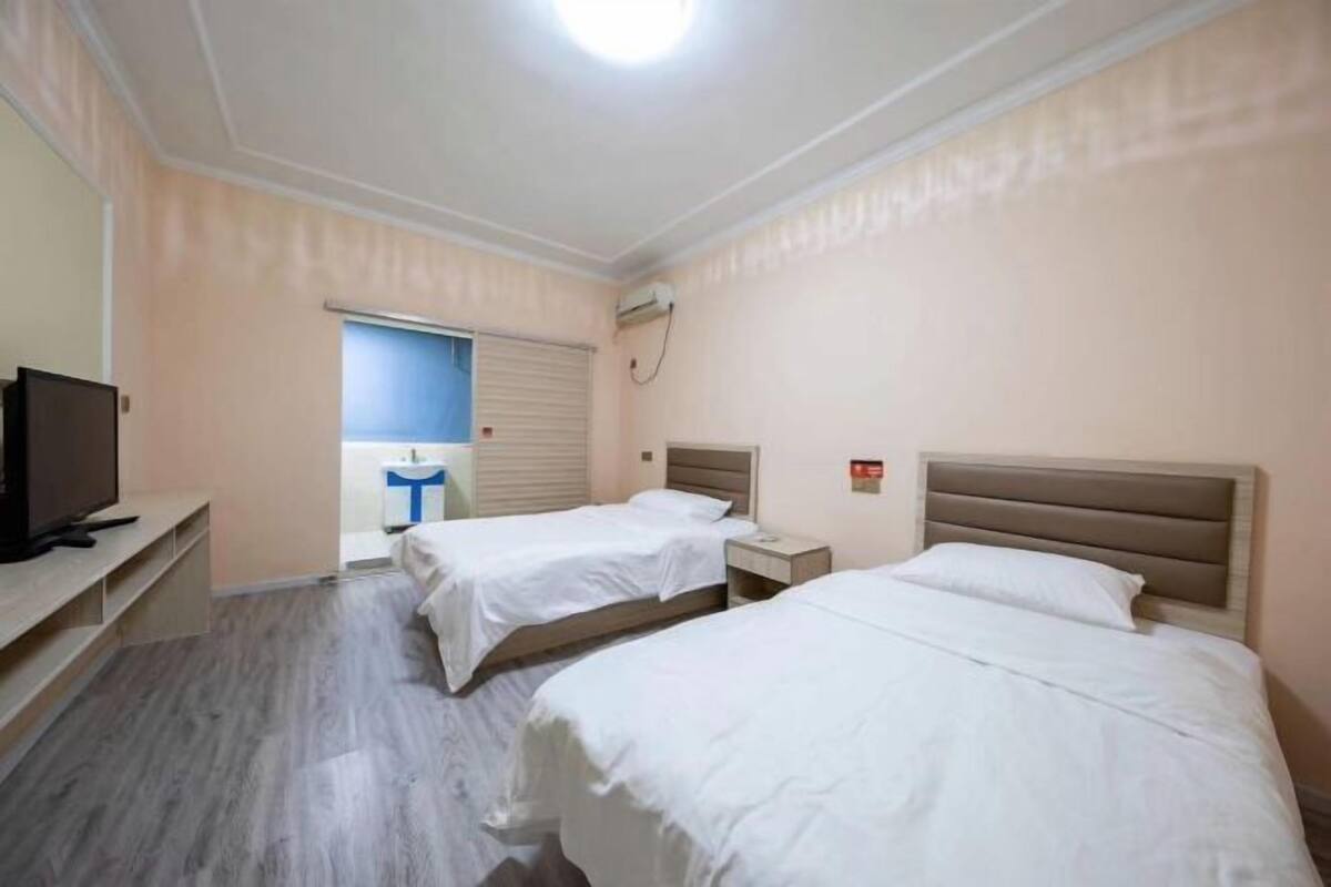 Habitación de hotel con dos camas, televisión, escritorio y ventana con persianas.