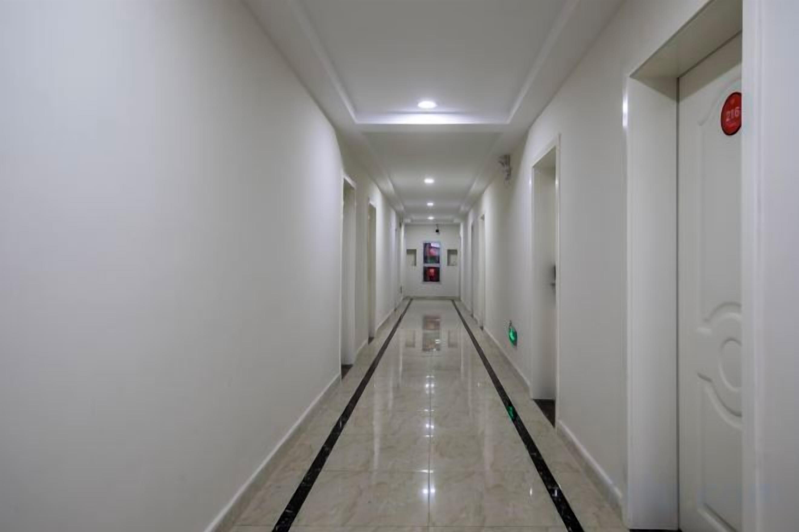 Un pasillo largo y estrecho con paredes blancas y un suelo brillante, que lleva a una puerta con un letrero rojo.