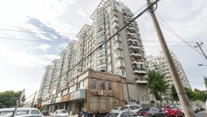 Un immeuble résidentiel à plusieurs étages, doté de balcons, avec des voitures garées et donnant sur la rue.