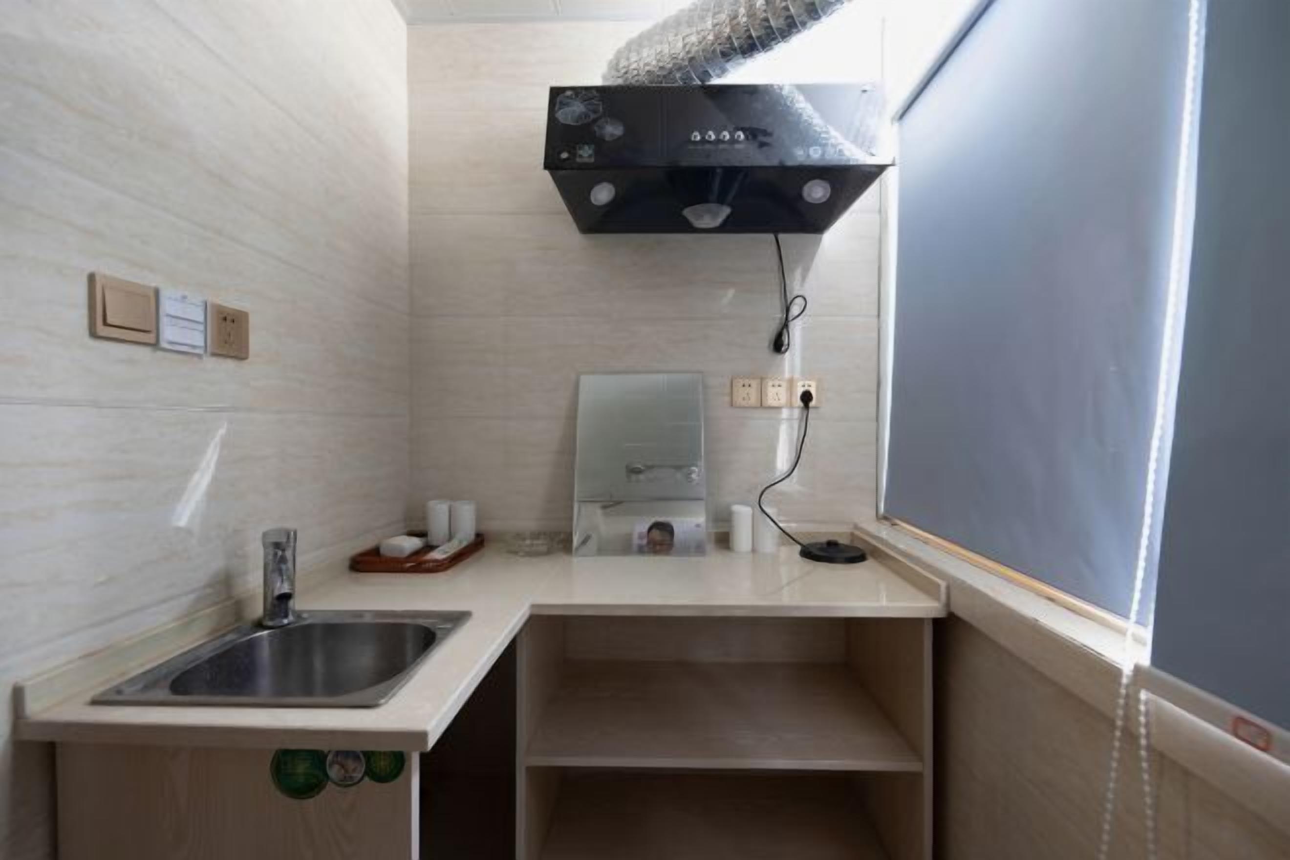 A bathroom with a sink, mirror, towel dispenser, and a shower area with a control panel.