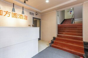 Zona de recepción de un hotel, con mostrador de recepción, una escalera y un letrero con el nombre del hotel.