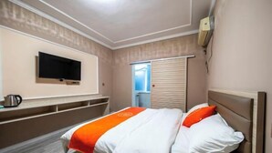 Une chambre d’hôtel équipée d’un lit, d’une télévision, d’une fenêtre avec stores et d’un climatiseur fixé au mur.