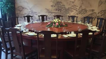 A round dining table set for eight with chairs, a floral centerpiece, and a traditional Chinese-style wall mural in the background.