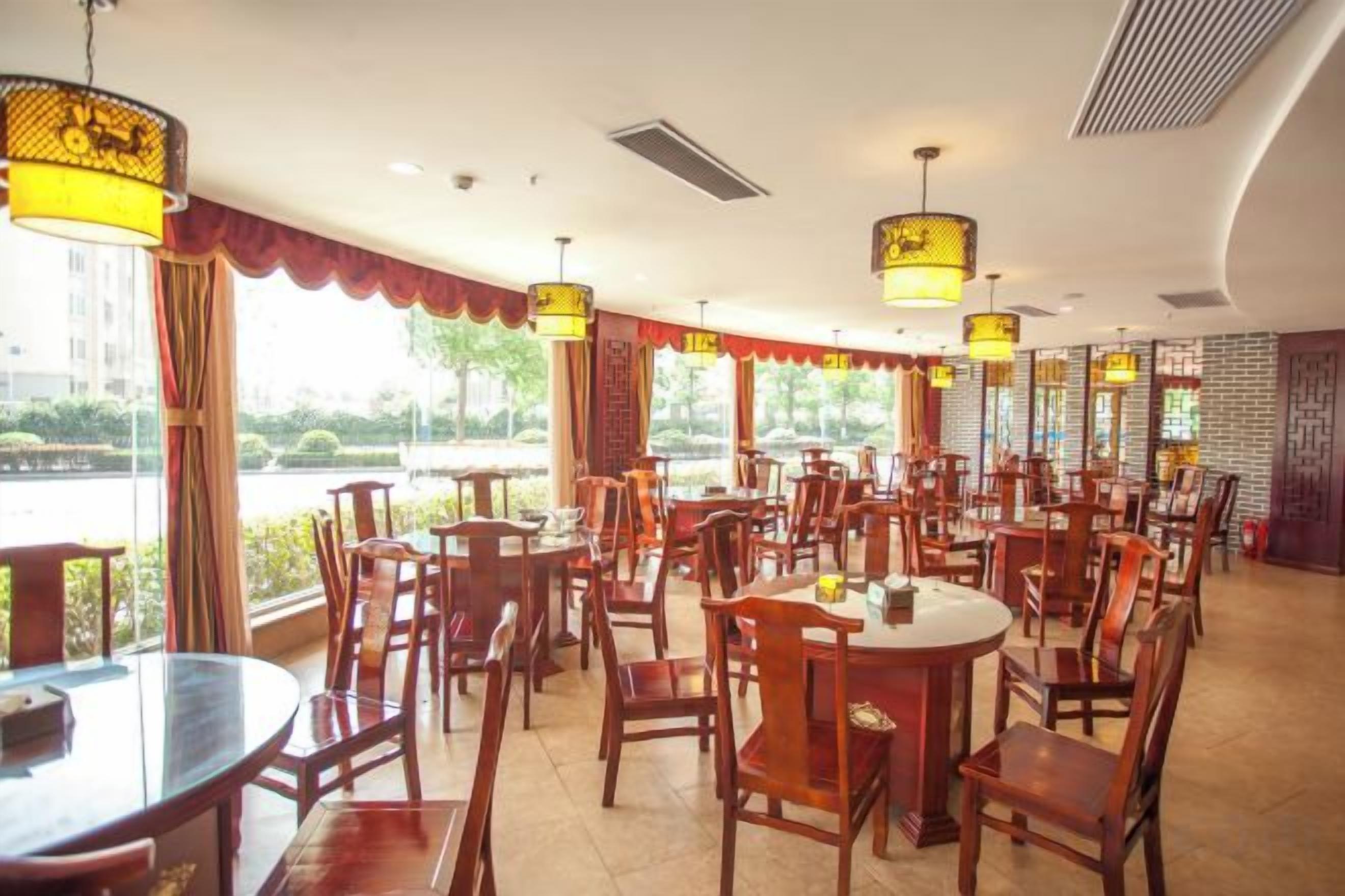 A restaurant with multiple tables and chairs, large windows, and hanging lamps.