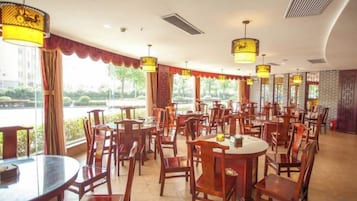A restaurant with multiple tables and chairs, large windows, and hanging lamps.