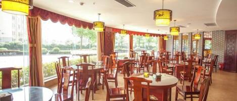 A restaurant with multiple tables and chairs, large windows, and hanging lamps.