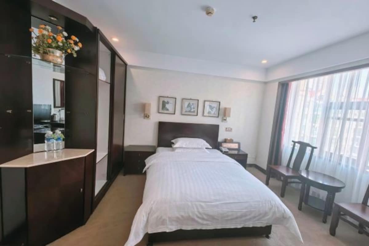 A hotel room with a large bed, a bedside table, a chair, and a window with curtains.