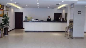 A hotel reception area with a reception desk, a potted plant, and a sign indicating a smoking area.