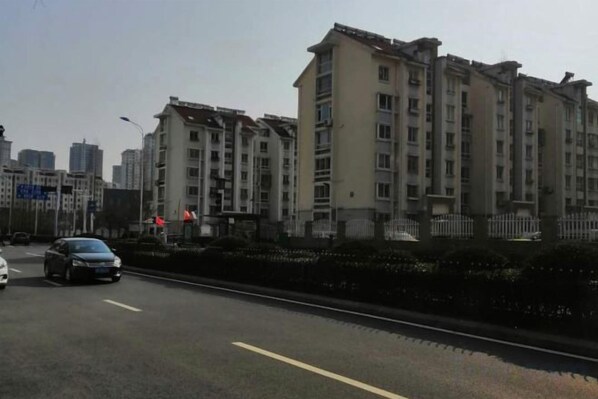Un edificio residencial de varios pisos con entrada protegida, una calle con vehículos y cielo despejado.