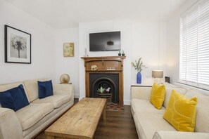 A living room with a fireplace, two sofas, a coffee table, and a television mounted above the fireplace.