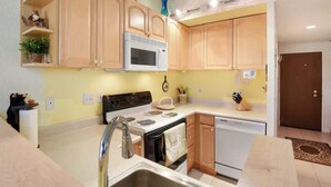 A compact kitchen with wooden cabinets, a microwave, a stove, and a dishwasher.