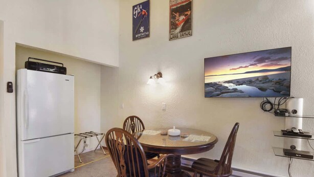 A compact kitchen with a refrigerator, dining table, and chairs. There are two wall-mounted posters and a painting above the table.