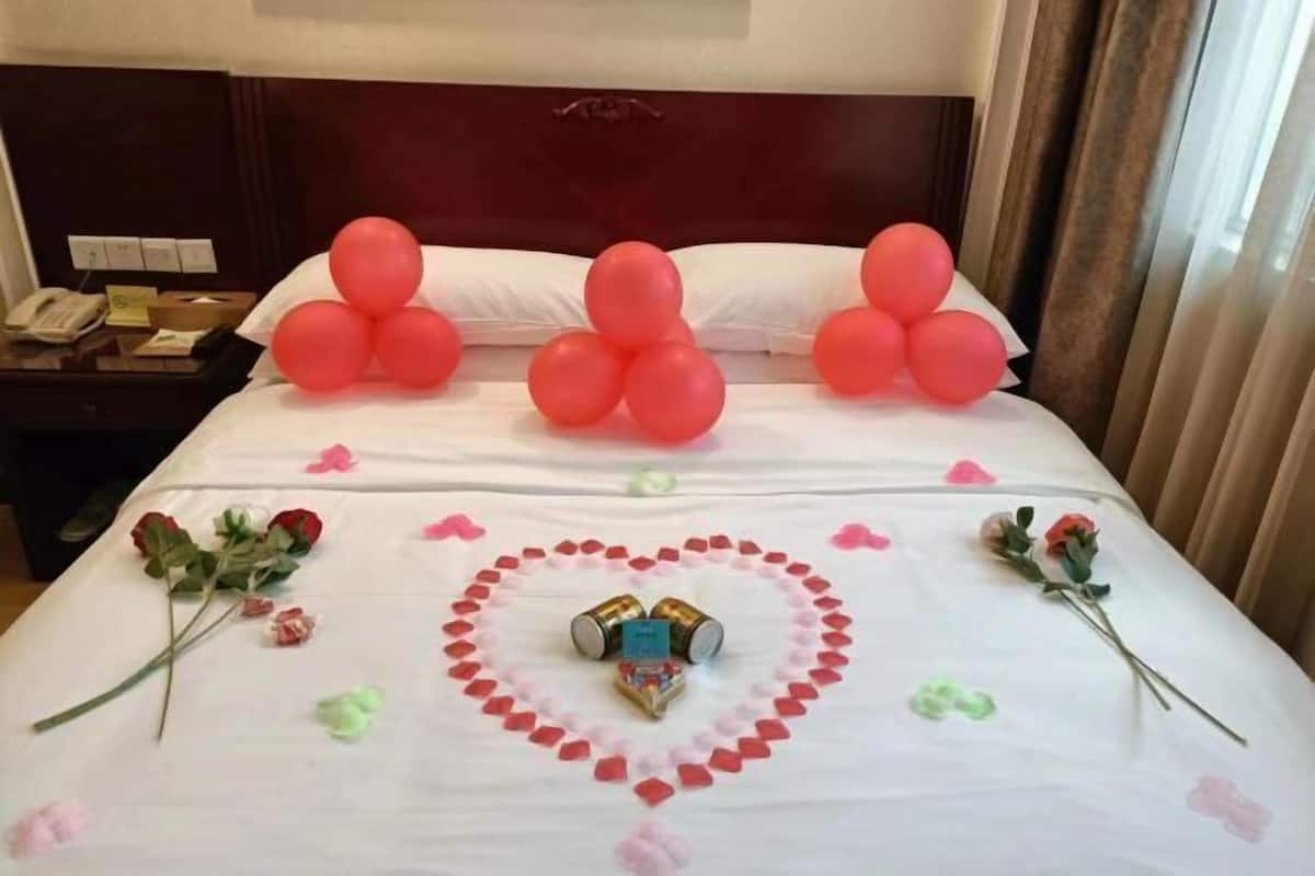 A hotel room with a neatly made bed, a bedside table with a phone, and a nightstand with a lamp.