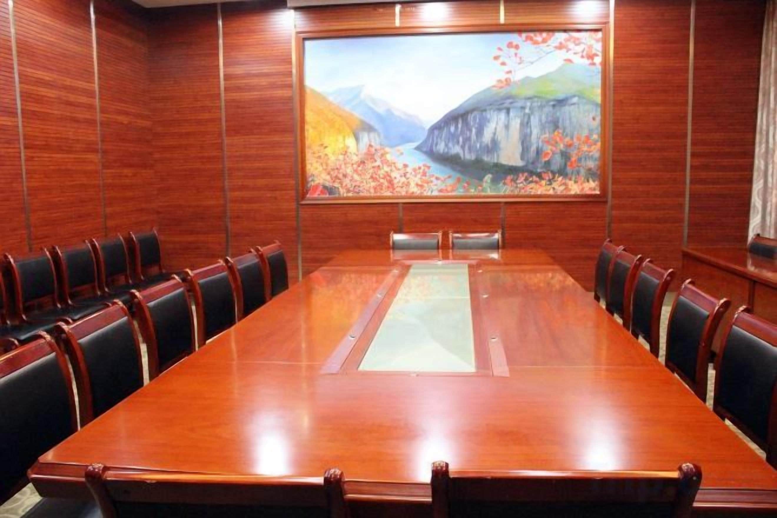 Uma sala de conferências com uma mesa comprida, cadeiras e uma tela grande exibindo uma imagem panorâmica.