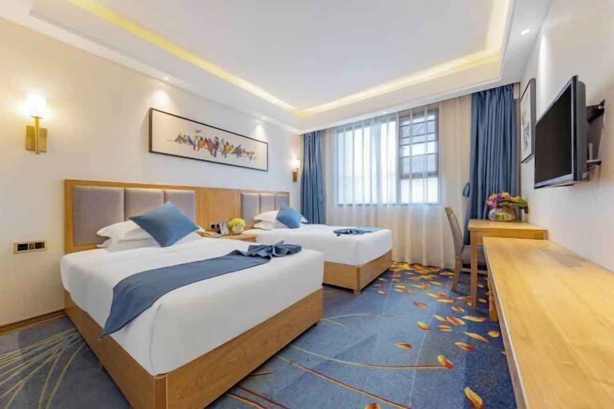 A hotel room with two beds, a desk, a flat-screen TV, and a painting on the wall.