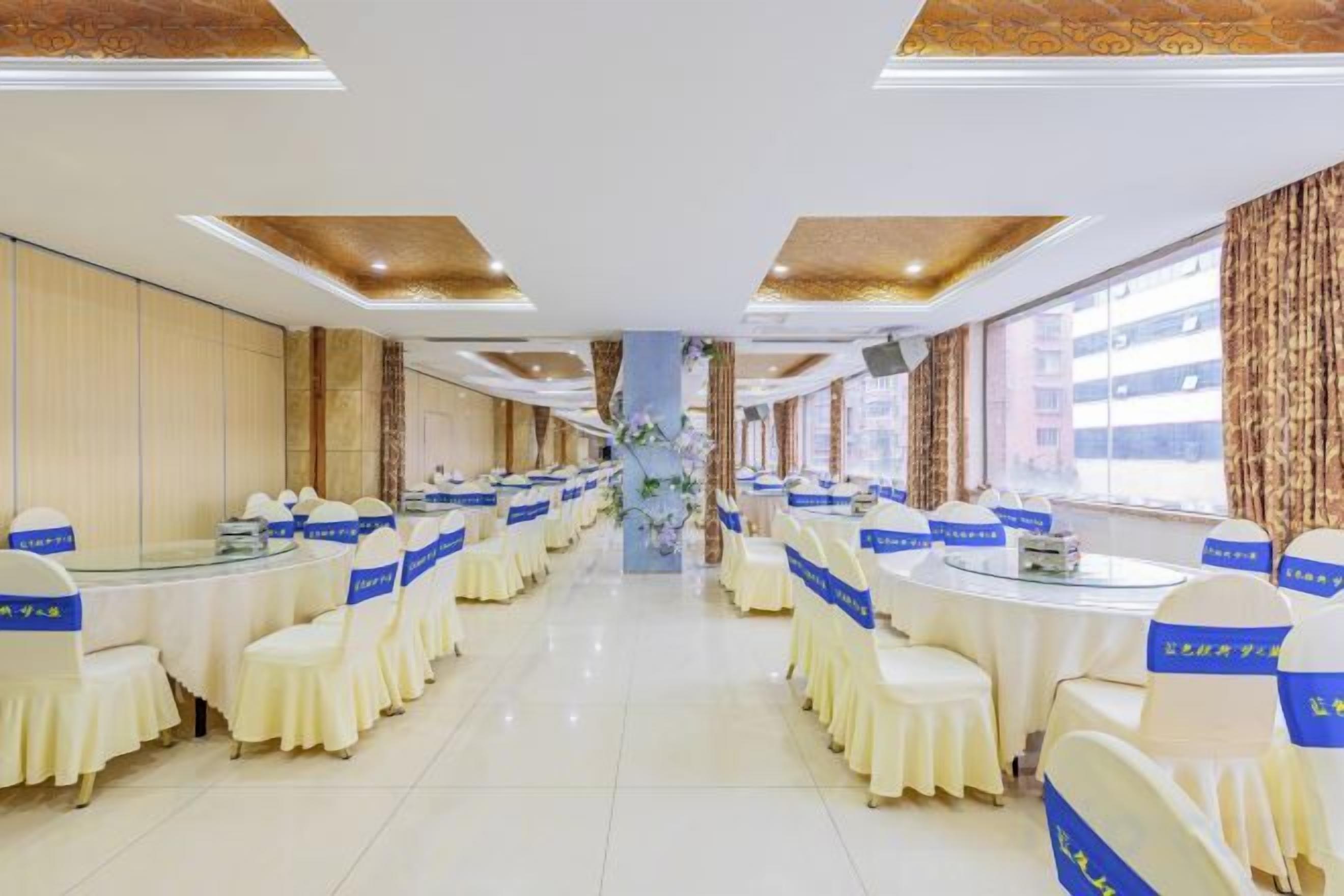 A banquet hall with round tables and chairs, a central floral arrangement, and a view of the city through large windows.