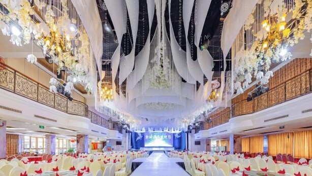 A banquet hall with rows of tables and chairs, a stage at the front, and decorative chandeliers. - Jincheng Hotel (Zigui)