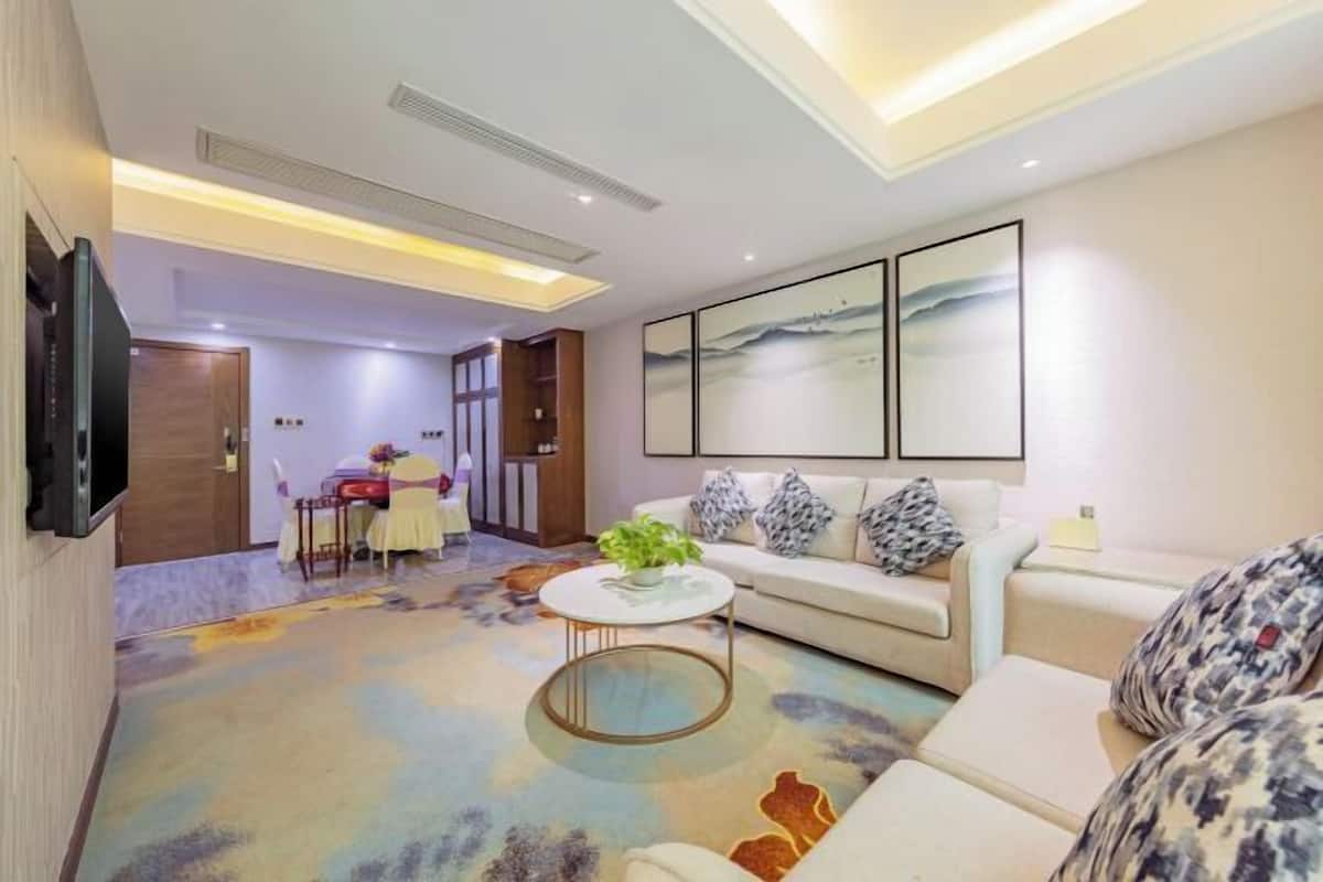 A modern living room with a sofa, a coffee table, and a TV mounted on the wall. There is a dining area with a table and chairs in the background.