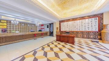A hotel lobby with a reception desk, a large wall with calligraphy, and a patterned floor.