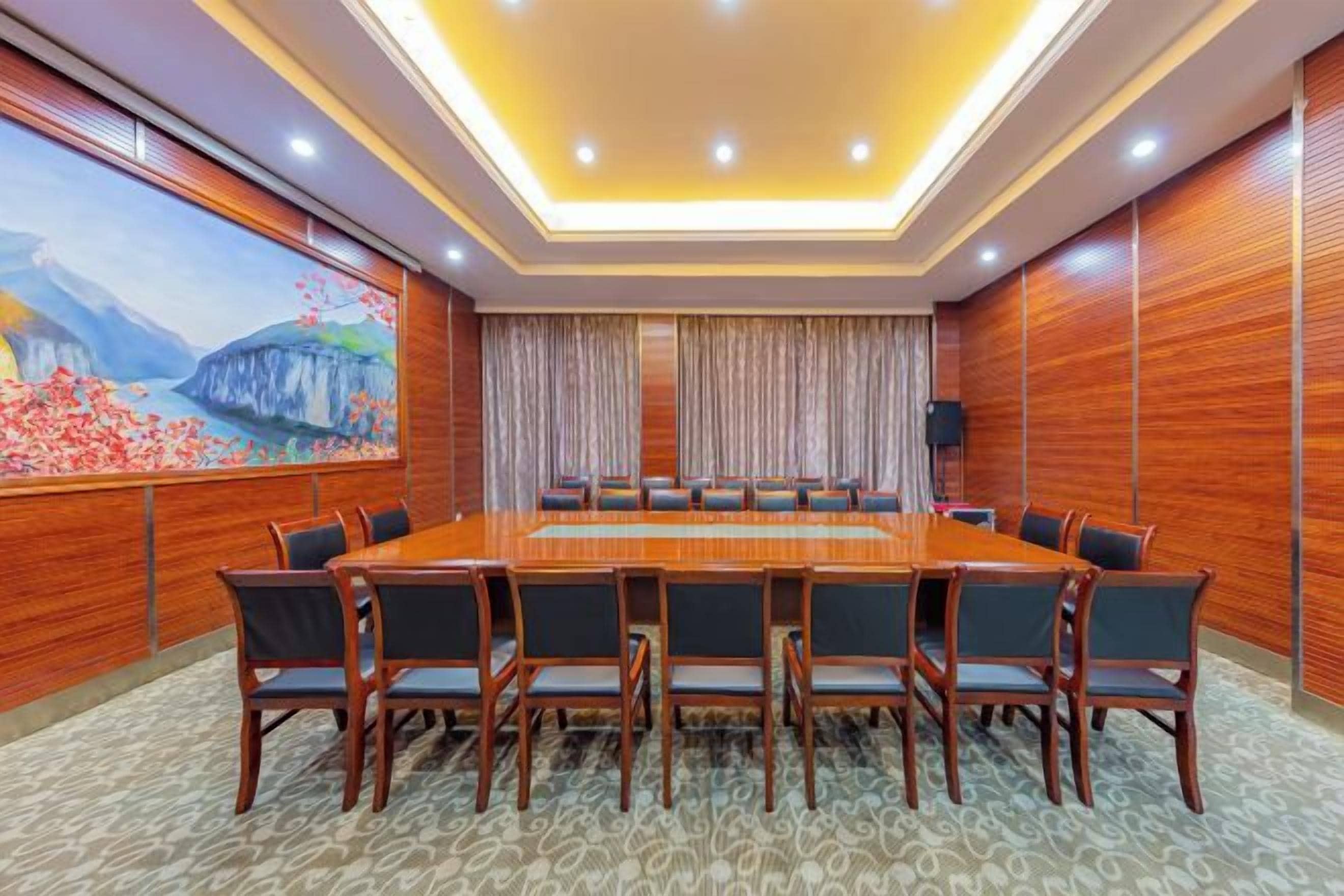 Un salón de conferencias con una larga mesa, sillas y un cuadro en la pared.