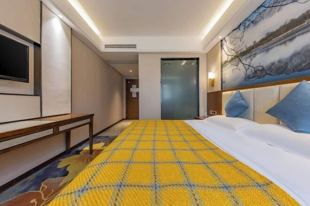 A hotel room with a bed, a television, a painting on the wall, and a cross on the door.