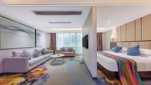 A modern hotel room with a sofa, a bed with a colorful blanket, a TV, and a large window with curtains. - Jincheng Hotel (Zigui)