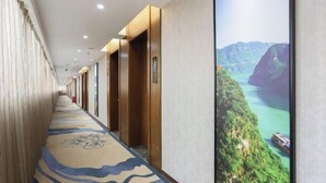 A hotel corridor with a patterned carpet, wooden doors, and a large wall-mounted screen displaying a scenic view. - Jincheng Hotel (Zigui)
