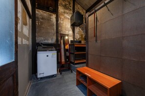 Quarto compacto com uma pequena geladeira, um banco de madeira e um armário fixado em uma parede texturizada.