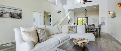 A spacious living room with a sectional sofa, a dining area with wooden chairs, a staircase, and a ceiling fan.