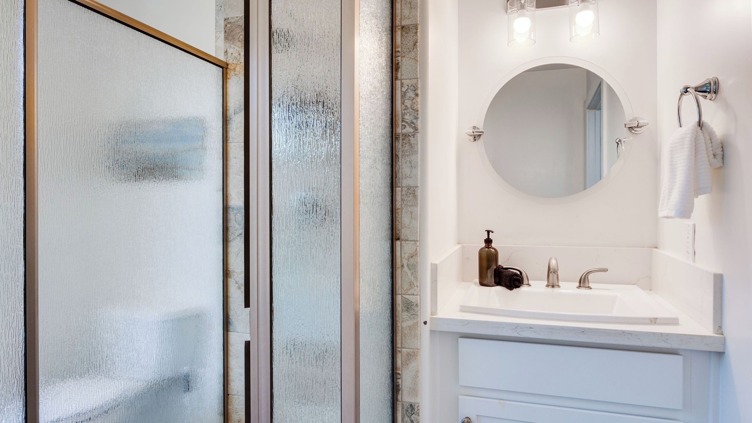 Un baño con cabina de ducha de vidrio, un lavabo blanco con un espejo redondo y un perchero para toallas.