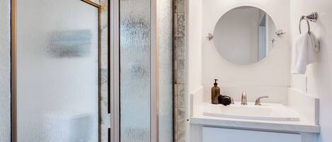 Un baño con cabina de ducha de vidrio, un lavabo blanco con un espejo redondo y un perchero para toallas.