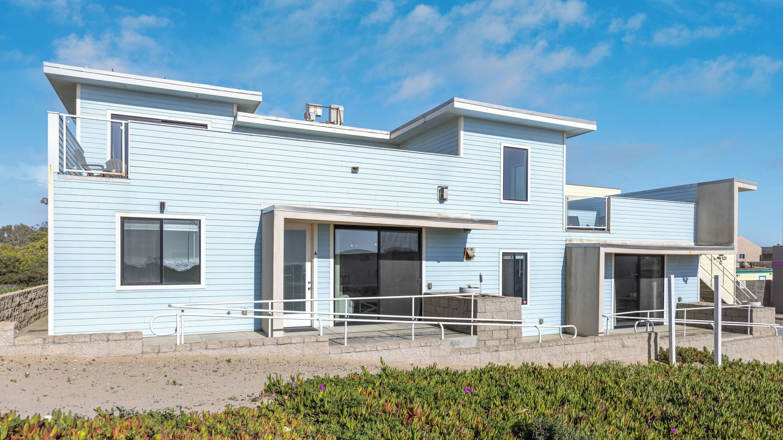 A modern two-story house with a flat roof, large windows, and a balcony.