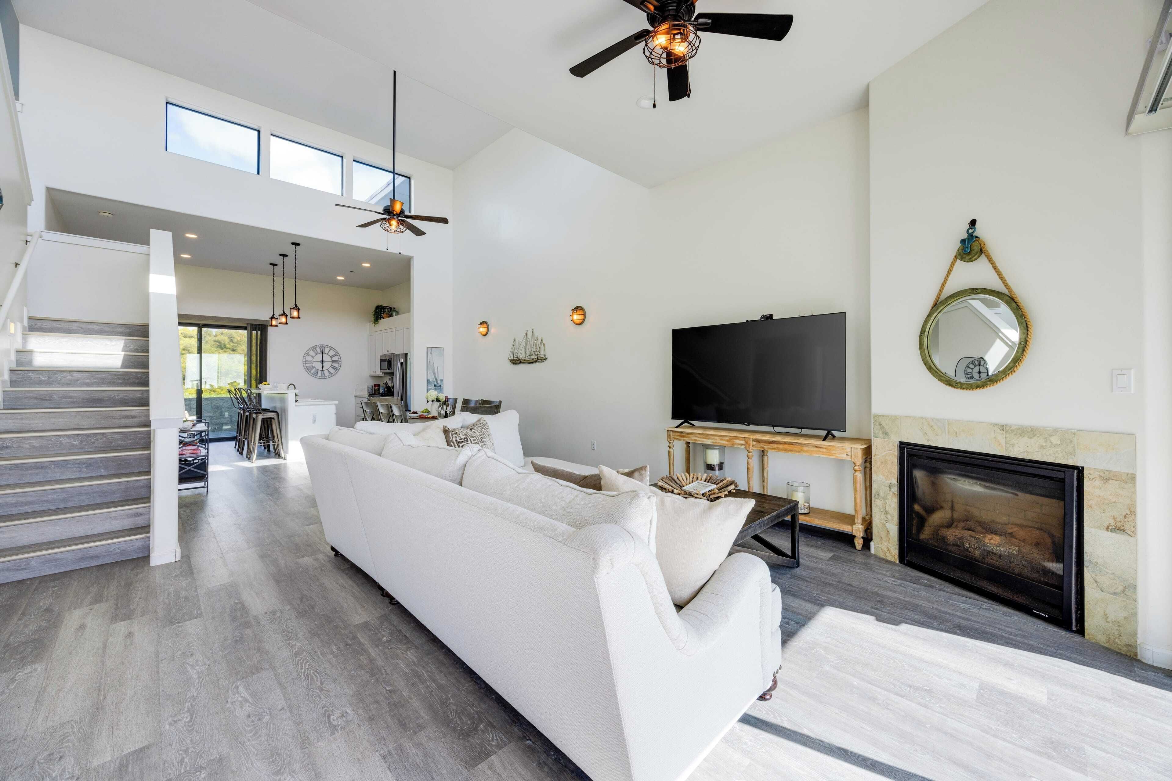 A spacious living room with a white sofa, a flat-screen TV, a fireplace, and a ceiling fan.