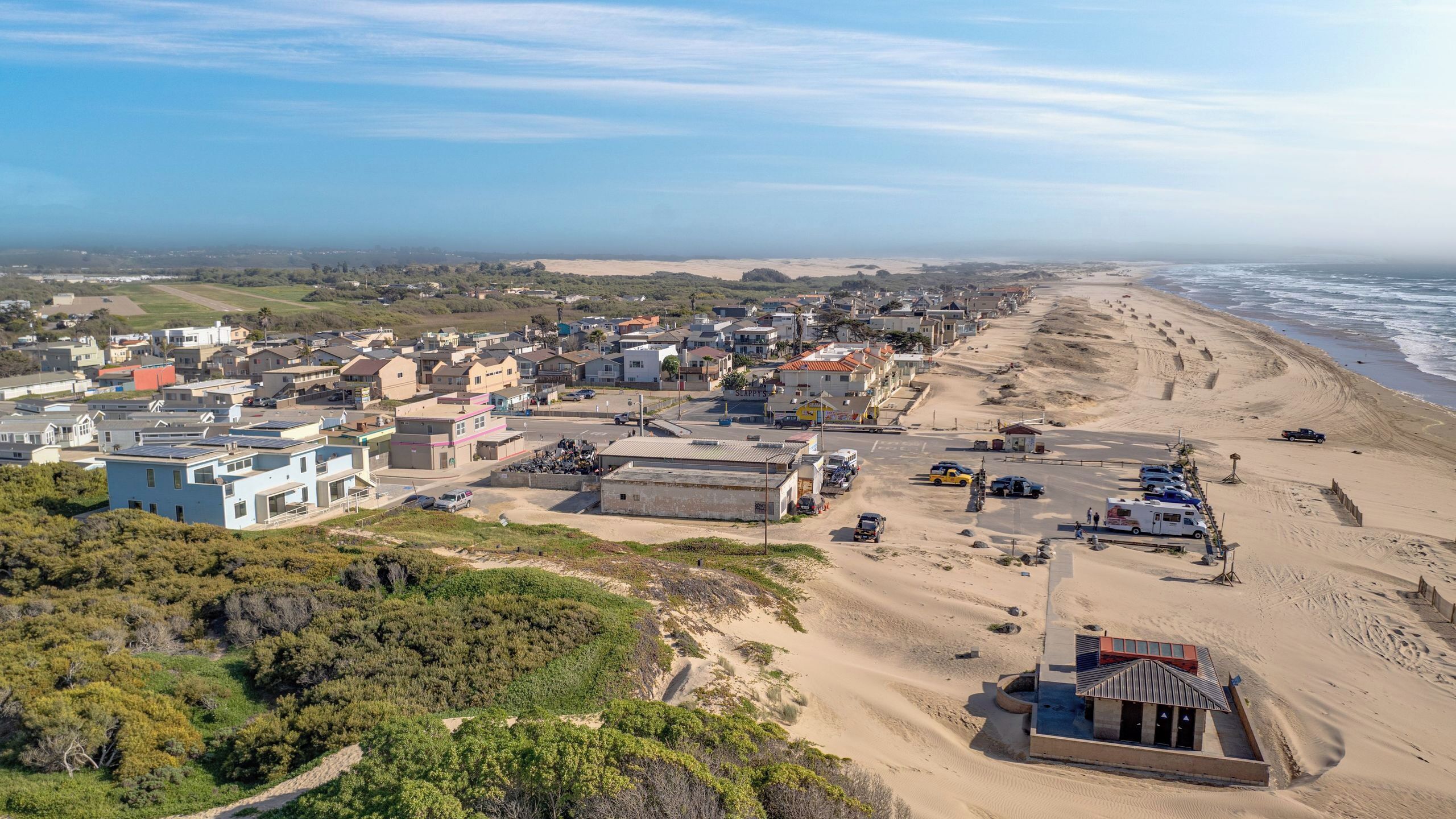 A coastal town with residential buildings, a sandy beach, and a small structure near the shore.