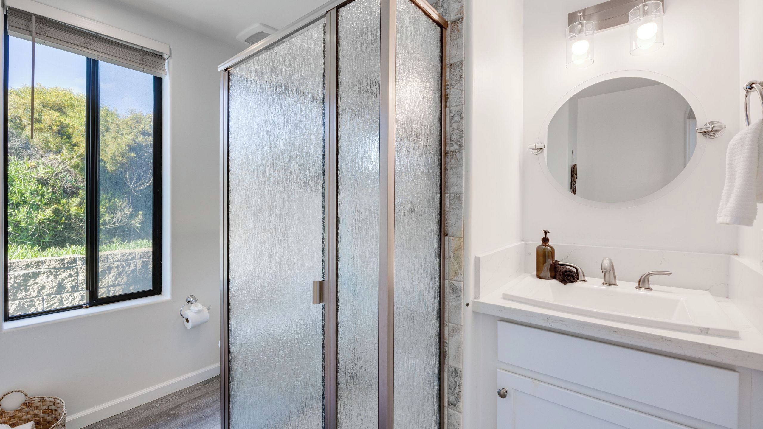 Une salle de bain avec une grande fenêtre, une douche, un lavabo avec un miroir et un porte-serviettes.