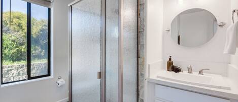Une salle de bain avec une grande fenêtre, une douche, un lavabo avec un miroir et un porte-serviettes.
