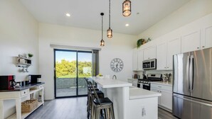 A modern kitchen with a central island, stainless steel appliances, and a large window overlooking greenery. - Beachfront 2BR w/ Deck, Views & Direct Sand Access Strand Way A (Oceano)