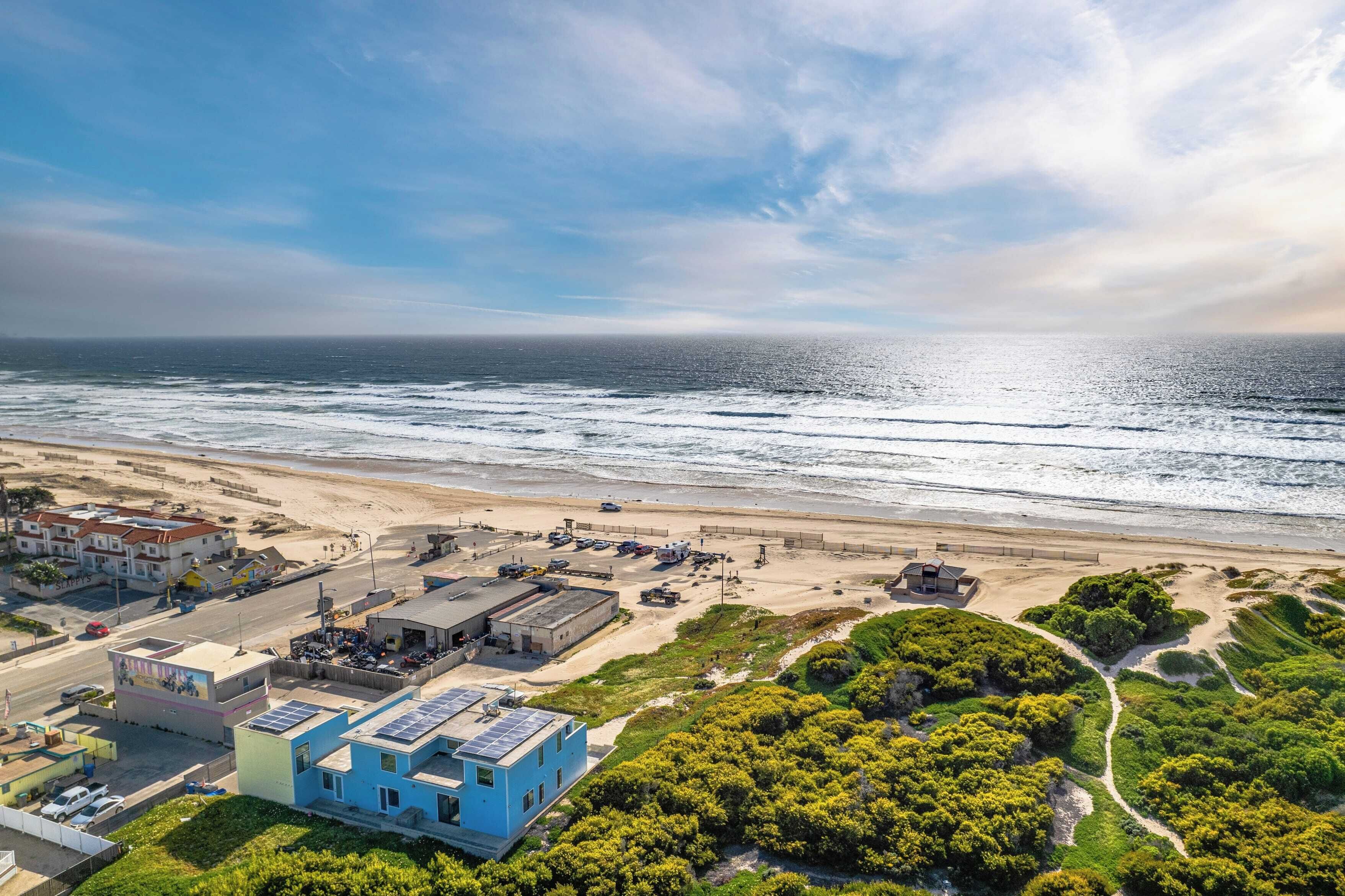 An aerial view of a coastal area with a beach, buildings, and greenery.