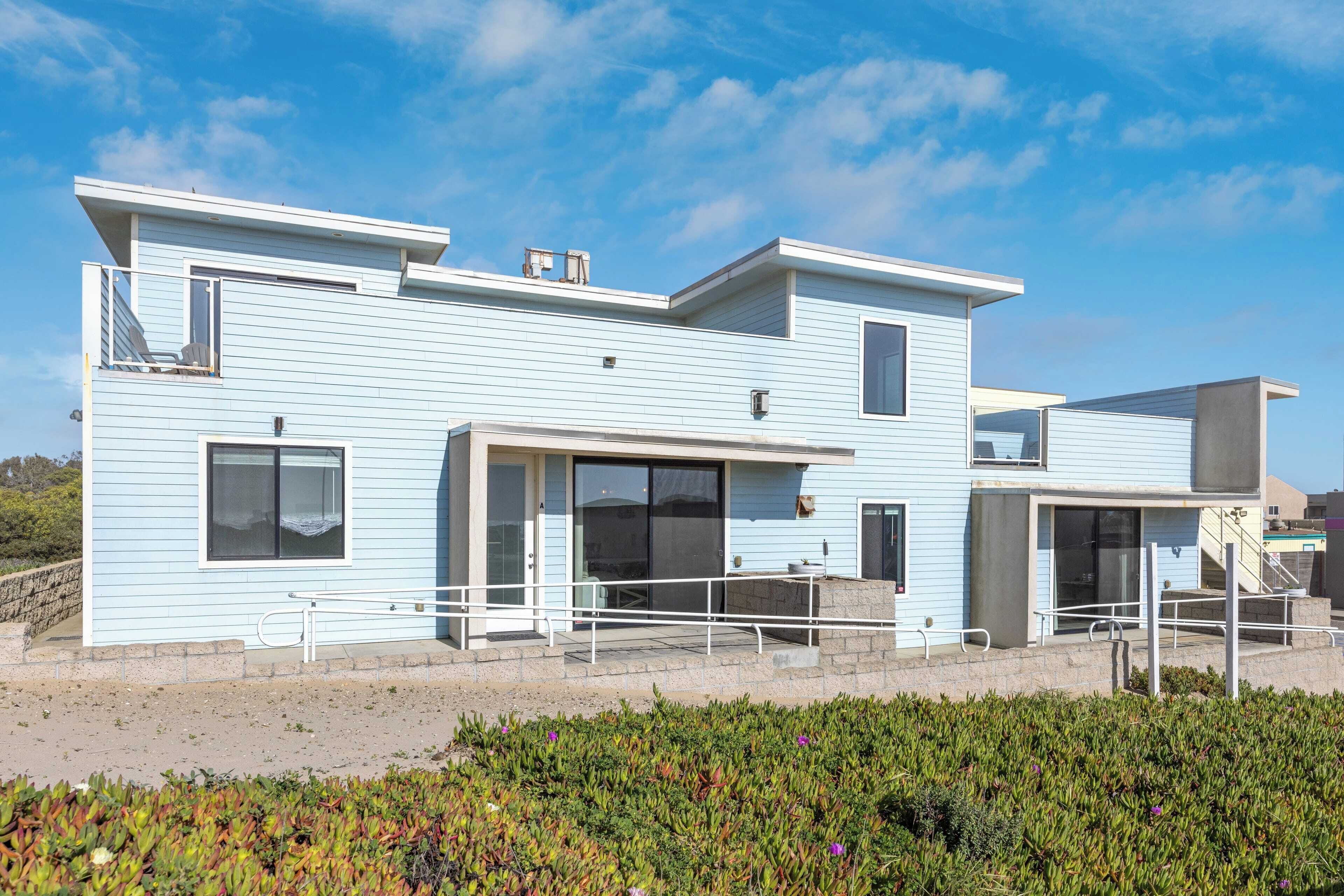 A modern coastal house with a flat roof, large windows, and a balcony.