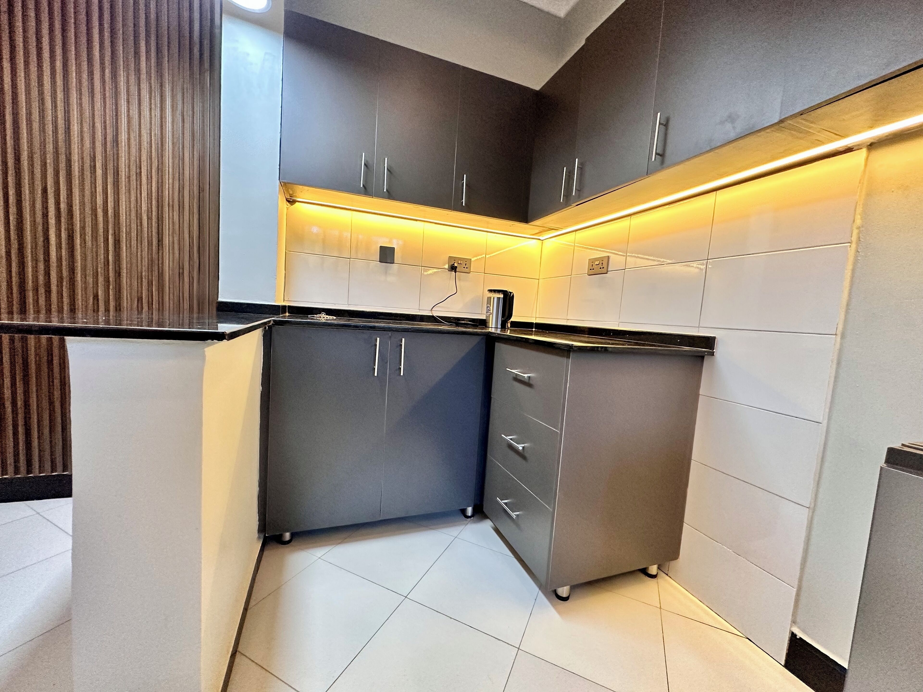 A modern kitchen with grey cabinets, a black countertop, and under-cabinet lighting.