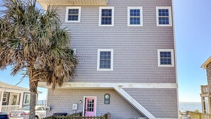 A multi-story building with a flat roof, a visible entrance with a pink door, and a small porch area with chairs. - Unbeatable Views & Coastal Charm (Harkers Island)