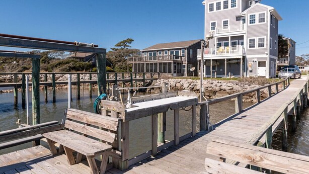 A wooden pier leading to a house with a balcony, a dock with a boat, and a clear blue sky. - Unbeatable Views & Coastal Charm (Harkers Island)